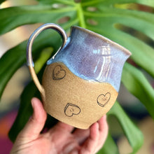 Load image into Gallery viewer, A handcrafted ceramic mug with a bluish-purple glaze and hearts with ASL slang written on them, held in front of a green plant.